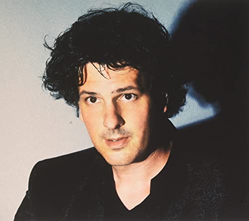 Close-up portrait of a man with dark curly hair, looking forward.