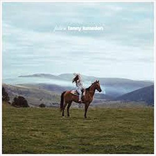A person riding a brown horse across a grassy field with mountains behind.