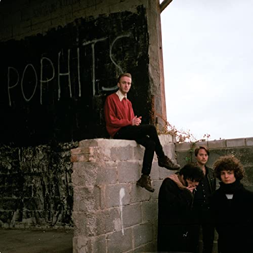 Band portrait with “POPHITS” graffiti on a concrete wall backdrop.