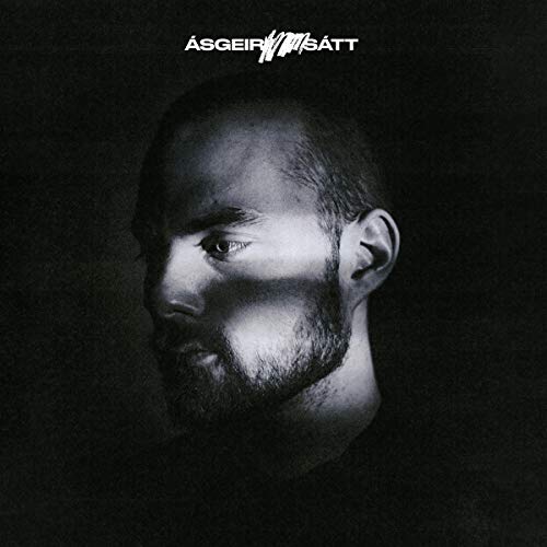 Black and white album cover with a man's face, partially shadowed, against a dark background.