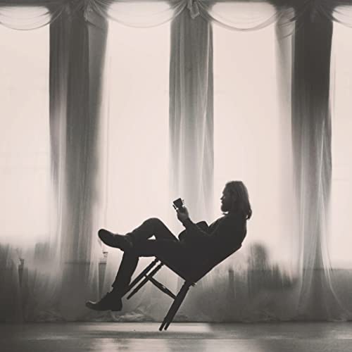 Black and white image of a person sitting with a guitar.
