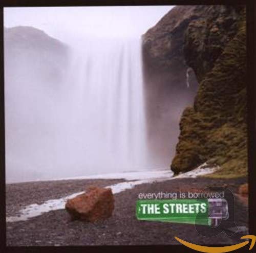 A large waterfall flows over a rocky cliff onto a dark, pebbled shore.