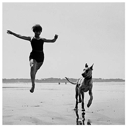 Black and white album cover: woman jumping with a running dog on a beach.