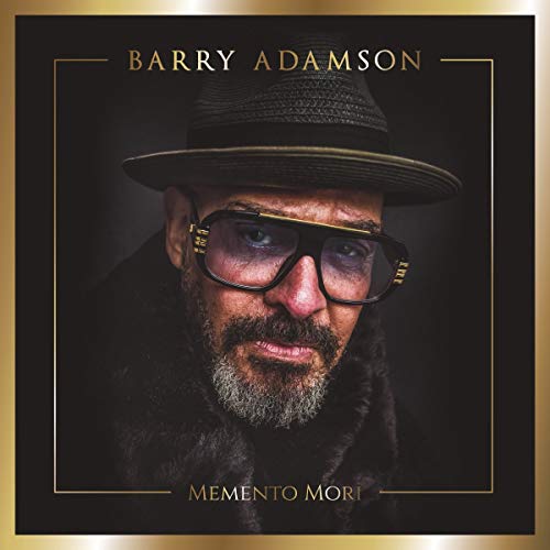Portrait of Barry Adamson wearing a hat and glasses against a dark background.