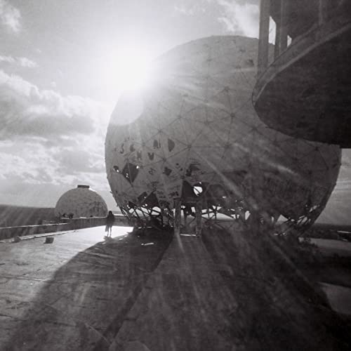 Black and white image of large, spherical radar domes against a cloudy sky.