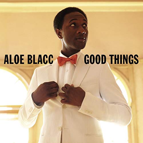 Aloe Blacc in a white suit and red bow tie, looking upwards.
