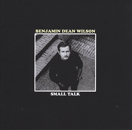 "Album cover with a black background, featuring a black-and-white photo of a man."