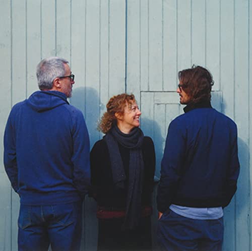 Three people, likely a musical trio, stand facing slightly away from the camera.