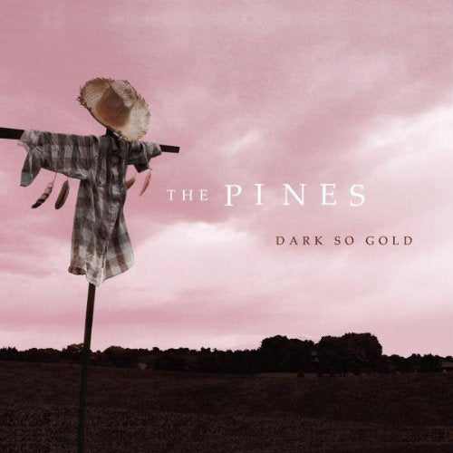 "Album cover: scarecrow in a field with pink sky, 'The Pines Dark So Gold'."