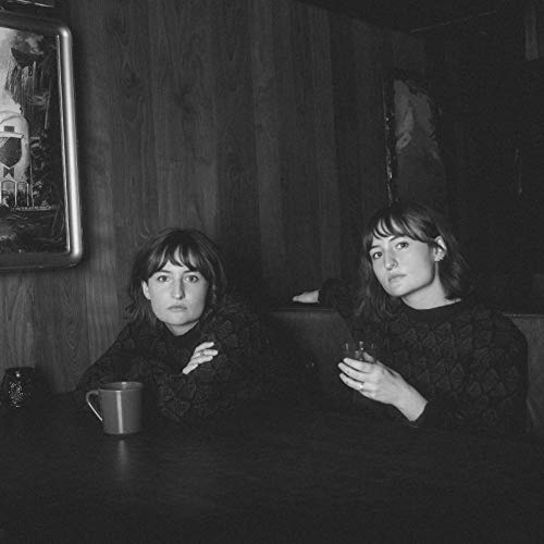 Black and white photo of a woman sitting at a table with a mug.