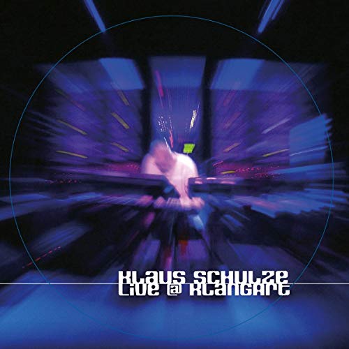 Blurry image of a musician at a synthesizer, dark blue and purple tones.