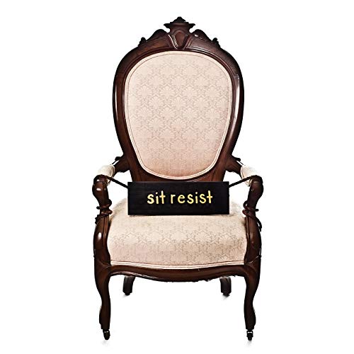 The image shows a dark wooden armchair with a beige upholstered seat and back. alt text: Dark wooden armchair with beige upholstery and "sit resist" sign attached.