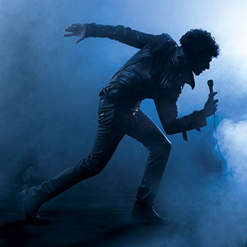 Man in leather suit singing into a microphone, smoky blue background.