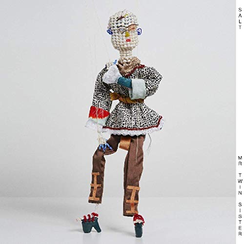 Marionette figurine with white pearl head, patterned dress, and brown pants against a white background.