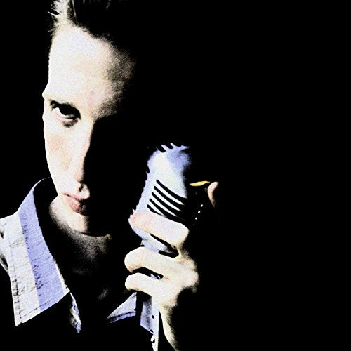 HighSSlightly high-contrast photo of a man holding a vintage microphone against a black background.