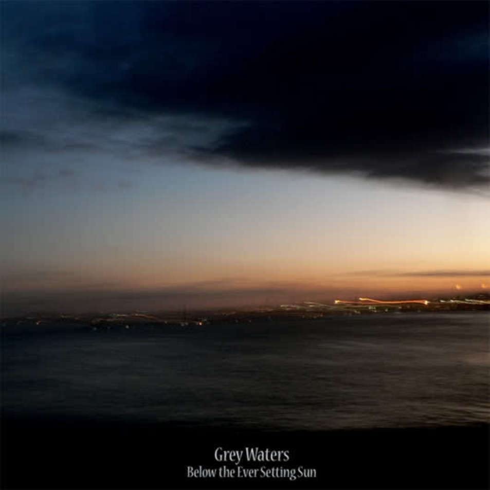 A sunset over a dark ocean with distant city lights under a cloudy sky.