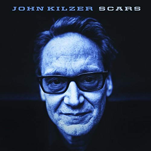 "Album cover with a blue-toned portrait of a man wearing glasses against a black background."