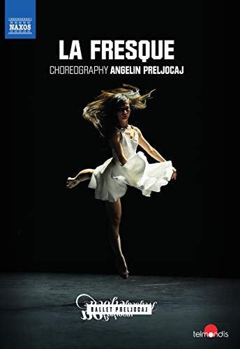 Ballet dancer in white dress mid-leap on a dark stage.