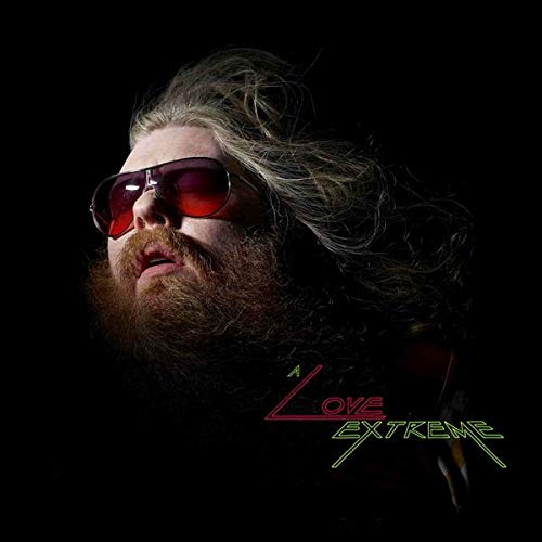 Close-up portrait of Benji Hughes with long hair, beard, and red sunglasses.