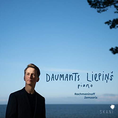 Man in black jacket stands before ocean, with text "Daumants Liepins piano" on the right.