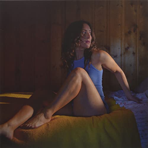 Woman with long dark hair sitting on a yellow bed.
