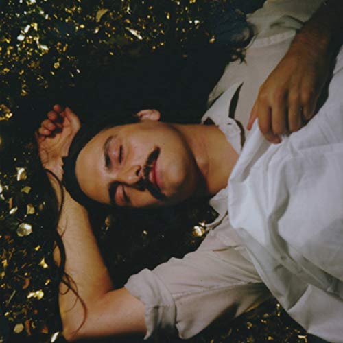 Woman lying among scattered confetti, eyes closed, album cover art.