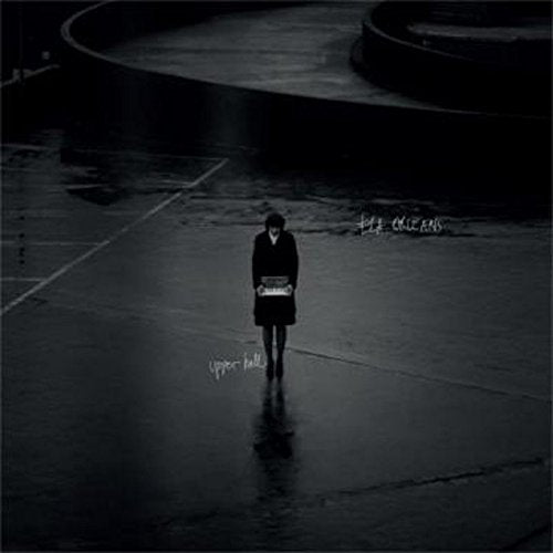 Lone figure stands on a wet, dark surface with album text.