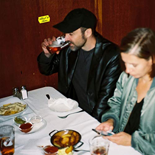 Man and woman at a table with food and drinks, album cover.