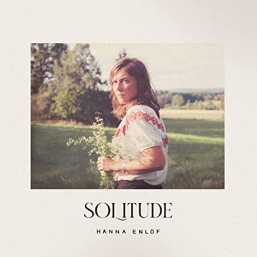 Woman holding flowers in a field, album cover for Hanna Enlöf’s “Solitude”.