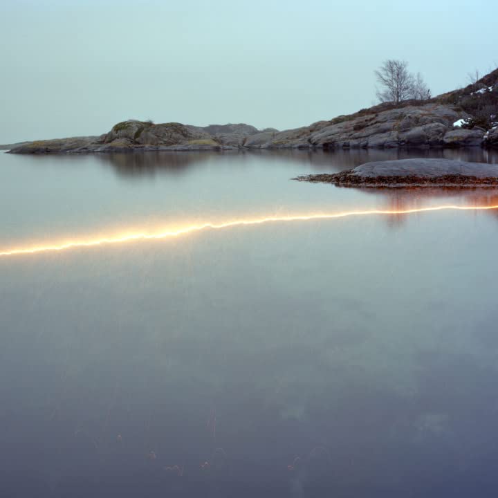 Coastal landscape with water, rocks, and a blurred orange light streak.