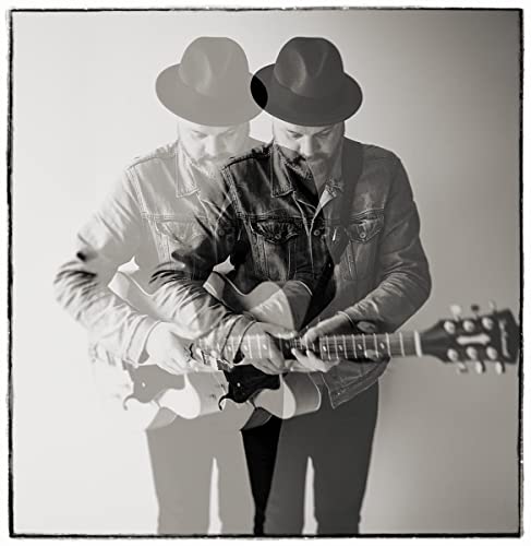 Black and white photo of a man with a guitar and hat.