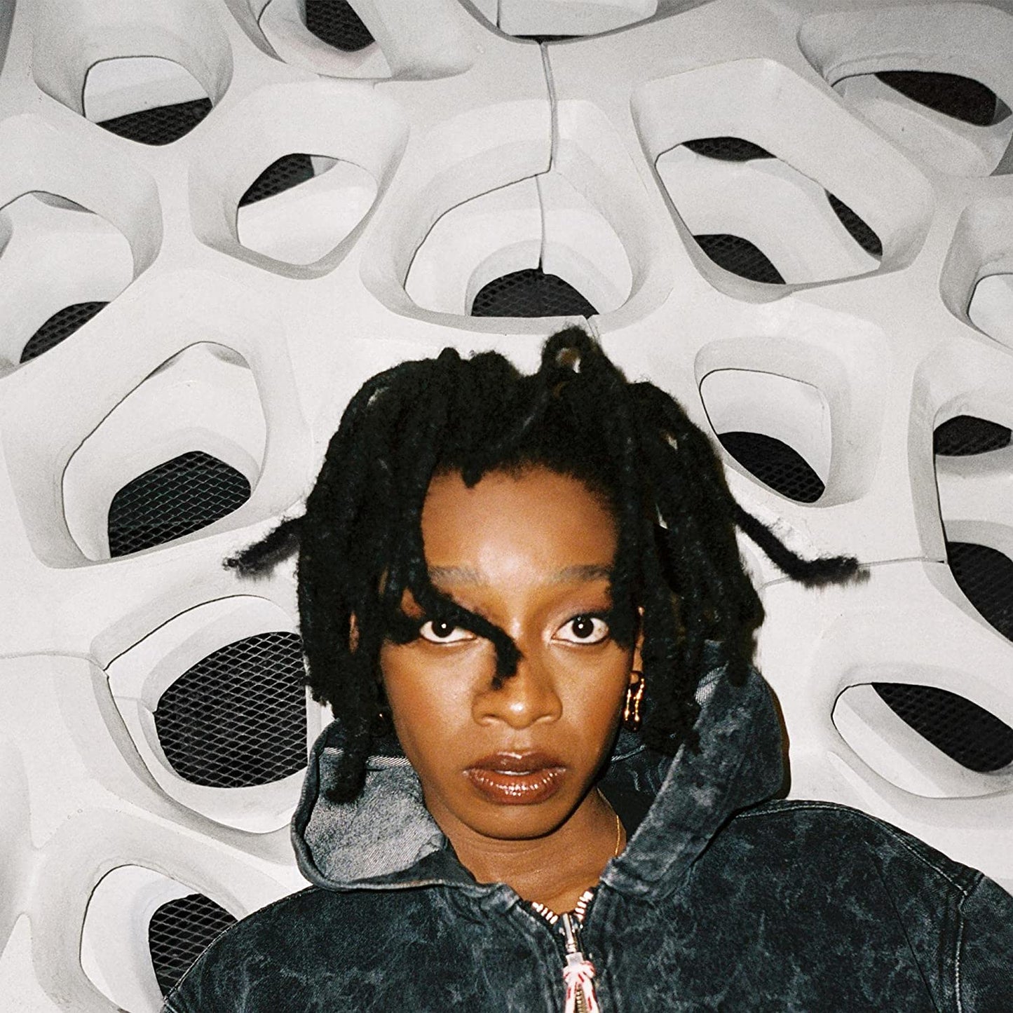 A woman with dark skin and dreadlocks gazes directly at the camera.
