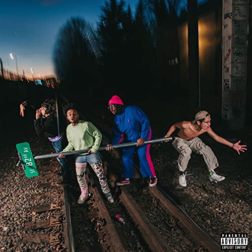 Four people on train tracks at dusk, album cover art.