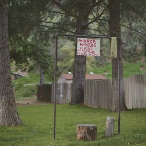 Sign reading "Mirror Woods" stands in a grassy, wooded area.