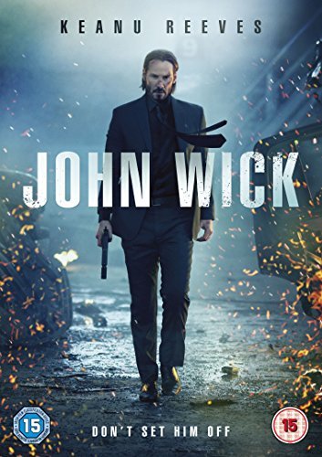 Keanu Reeves in a suit holding a gun, walking through a smoky, fiery scene.