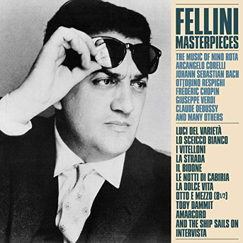 The image depicts a black and white photograph of a man in a suit, with the title "Fellini Masterpieces" written in large blue letters on the right side. The man is wearing a dark suit jacket, a white shirt, and a tie, and is holding a pair of sunglasses up to his face. The background of the image is a light beige color. The text on the right side of the image lists the names of various songs and artists, including "Luci del Varieta"