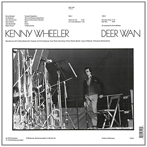 Black and white vinyl record cover with a man standing among microphones on stage.