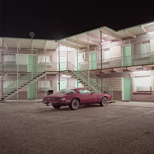 Red car parked in front of a two-story motel at night.