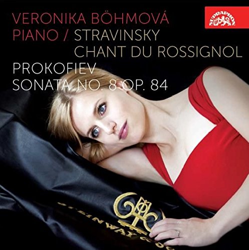 A woman in a red dress lies beside a piano with a black cover.