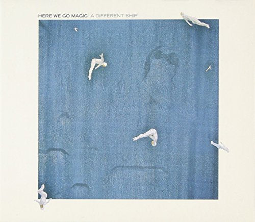 The image depicts a blue square with a white border, featuring a central design that appears to be a stylized representation of a ship. The square is surrounded by a white border, and the title "HERE WE GO MAGIC: A DIFFERENT SHIP" is displayed at the top. * The blue square has a white border around it. * The border is thick and uniform, providing a clear distinction between the square and the surrounding area. * The title "HERE WE