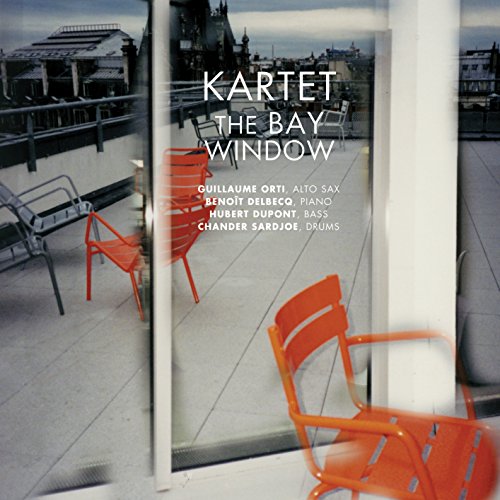 CD cover with blurred cityscape reflected in a window and red chairs.