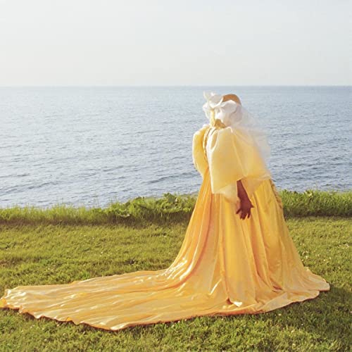 Person in flowing yellow garment stands with back to ocean.