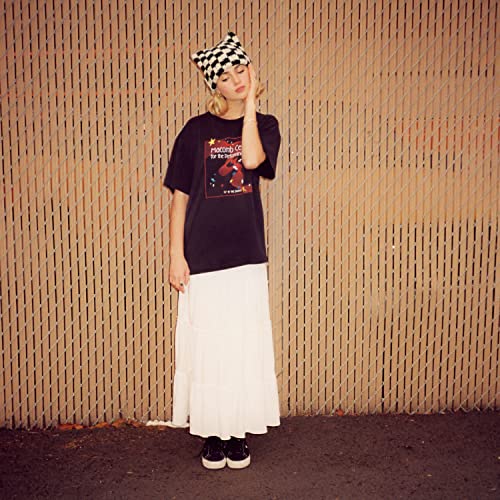 Woman in black shirt and white skirt posing against a wooden wall.