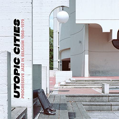 A person's legs sit on concrete steps in front of modern white architectural buildings.