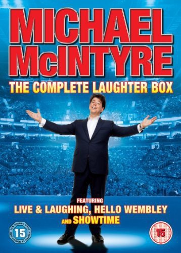 Michael McIntyre in a black suit stands with arms outstretched on a stage.