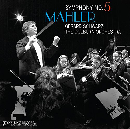 The image depicts a black-and-white photograph of a conductor leading an orchestra. Alt text: Conductor in tuxedo leads seated musicians playing string instruments, black-and-white image.