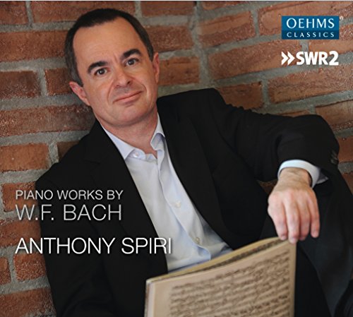Man in a black suit holding sheet music against a brick wall.