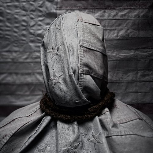 A hooded figure in a denim jacket against a dark, crumpled background.