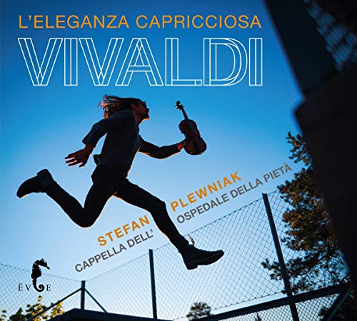 Man in black jumps in mid-air, holding a violin, against a blue sky.