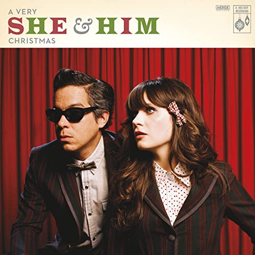 She and Him posing in matching striped blazers against a red curtain background.